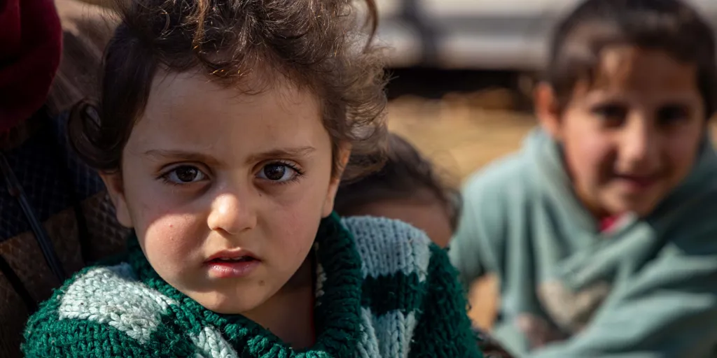 Child wearing a green jumper and looking at the camera